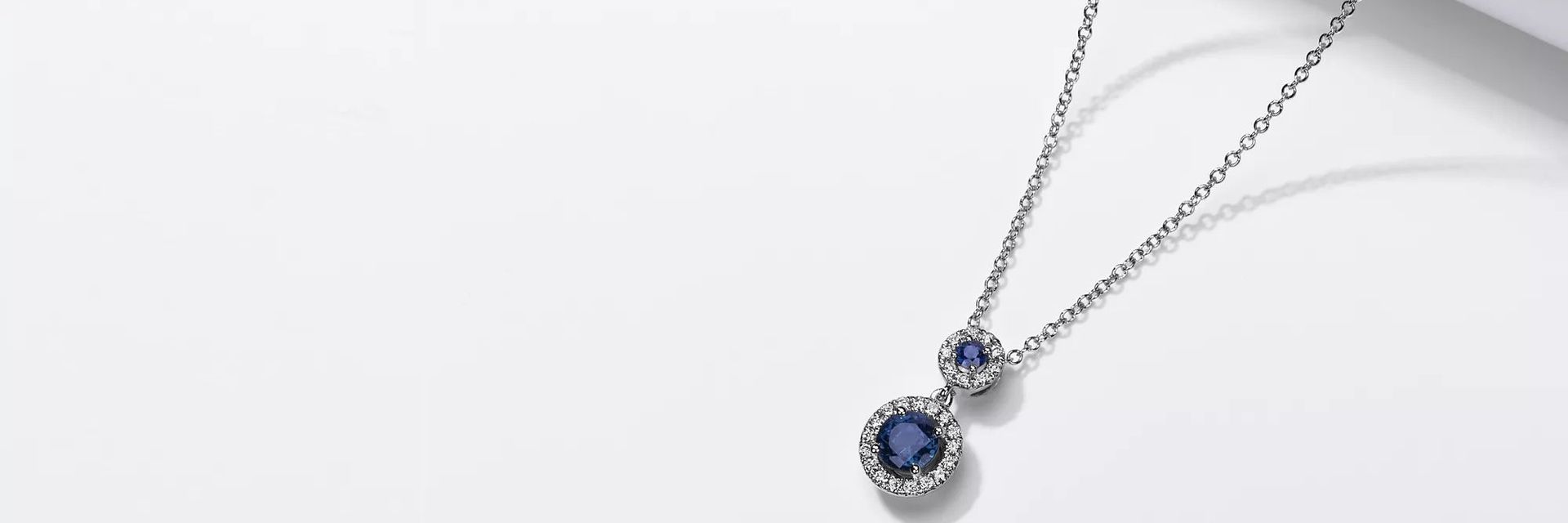 14k white gold pendant featuring two sapphires surrounded by diamond halos.